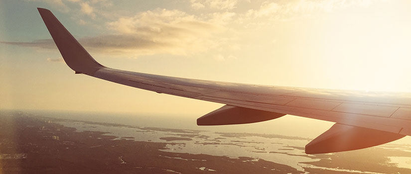 Sunset photo of an airplane wing in flight over coastal waters
